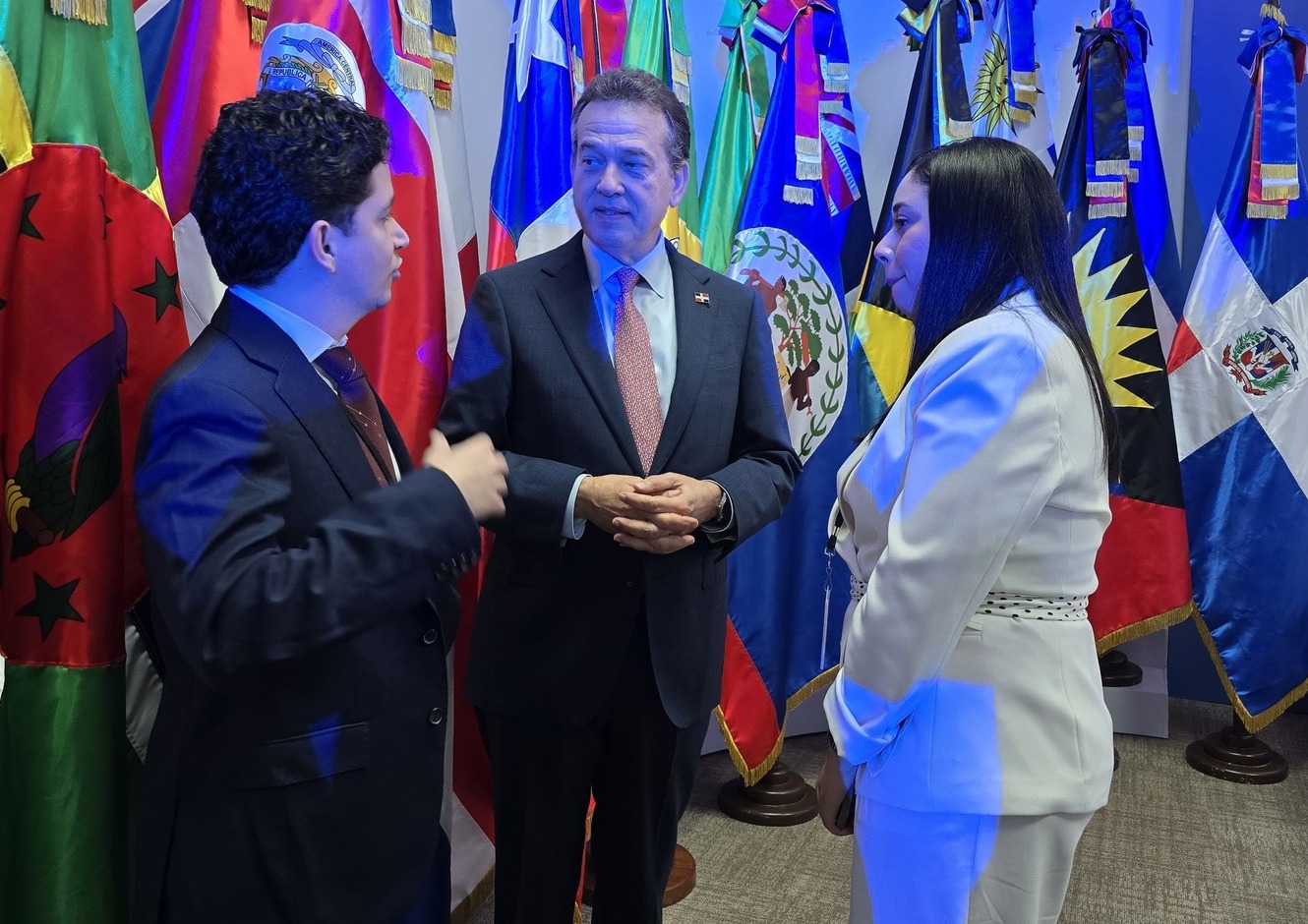 El canciller Víctor Orlando Bisonó conversa con Luisangela Solórzano, de la Coalición por Venezuela, y con el director del OLDS ante las banderas de los países miembros de la CEPAL